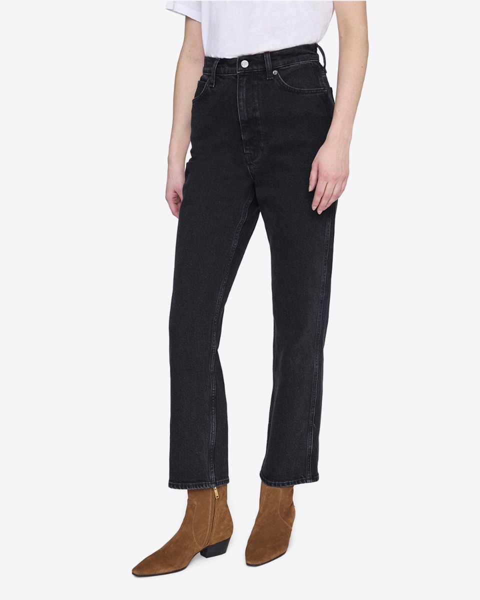 Jean taille haute Jane Anine Bing en denim noir vintage, port&eacute; de face avec des boots camel.