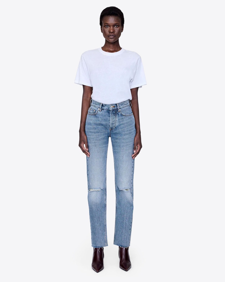 Jean taille haute slim Bruno Anine Bing en denim régénératif bleu déchiré aux genoux et porté de face.