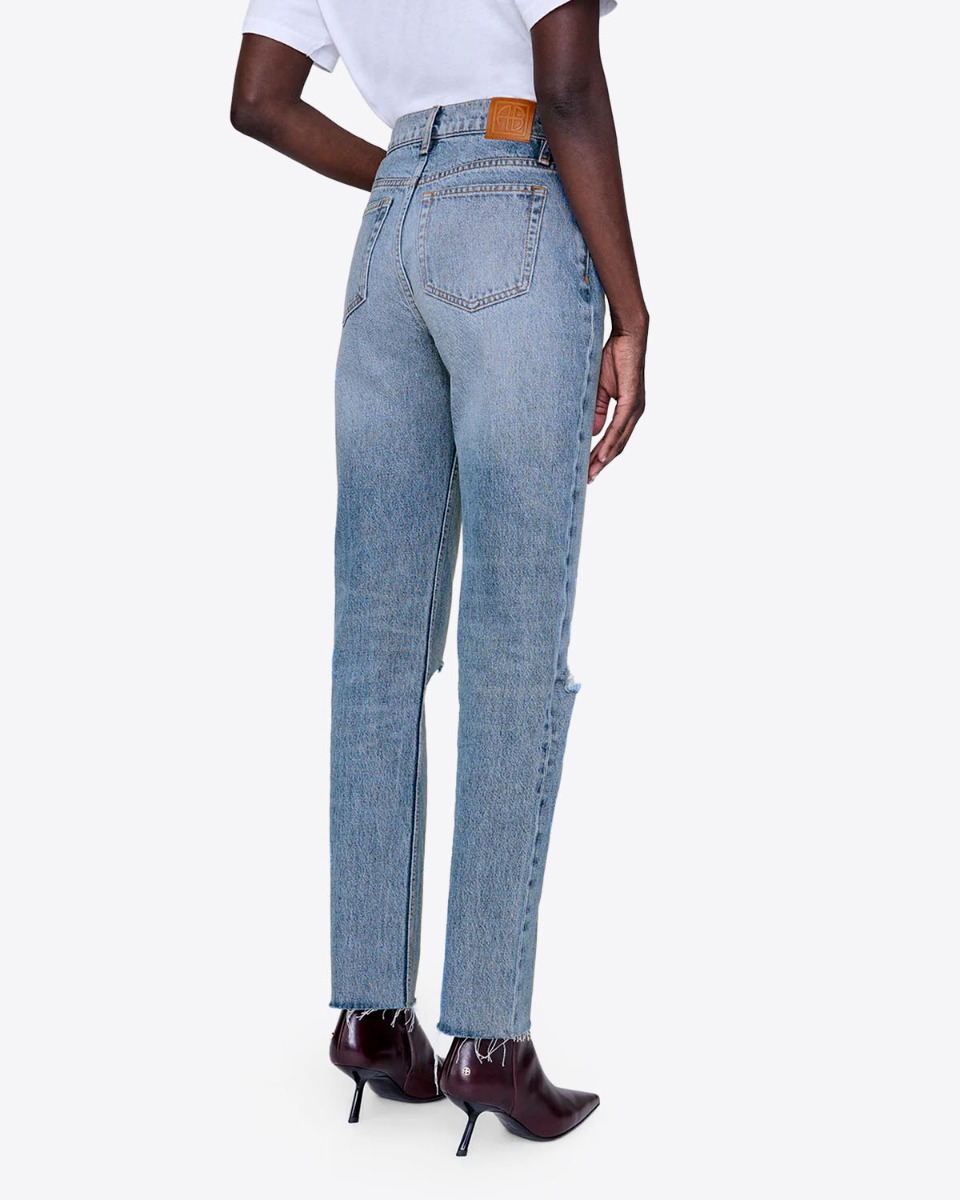 Jean taille haute slim Bruno Anine Bing en denim régénératif bleu déchiré aux genoux et porté de dos.