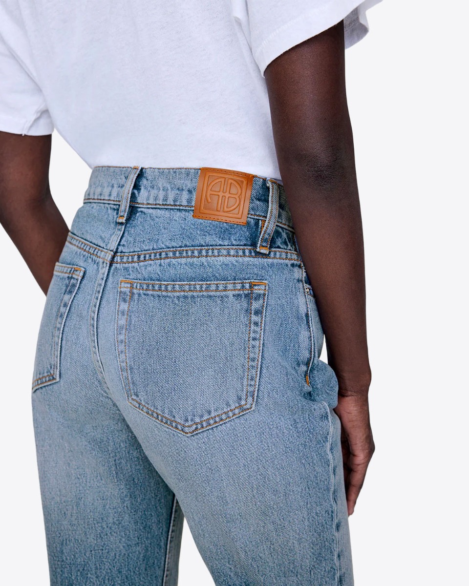 Jean taille haute slim Bruno Anine Bing en denim régénératif bleu déchiré aux genoux. Détail du dos avec le logo AB.