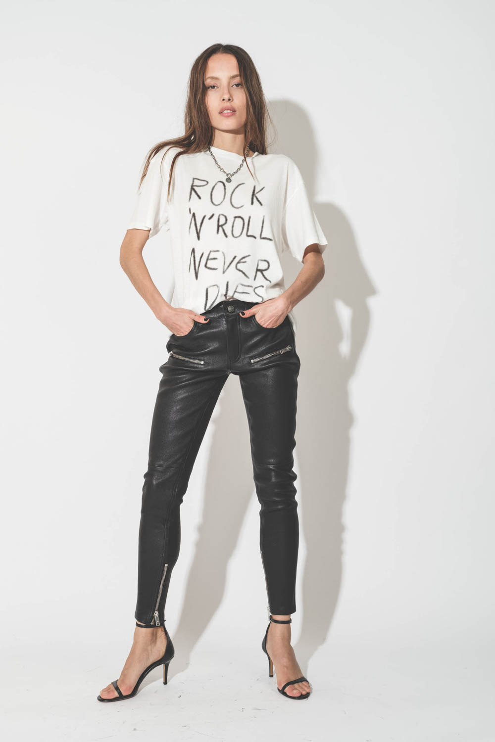 Pantalon skinny en cuir noir avec des zips aux poches et bas de jambes Remy Anine Bing. Porté avec des sandales à talons.