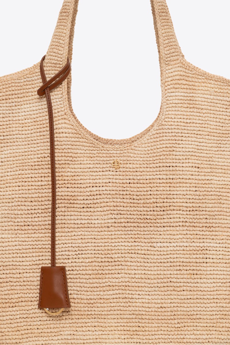 Sac cabas Lili Tote Anine Bing en raphia naturel. Détail du mini-logo « AB » doré sur le devant et du lien porte-clefs en cuir marron.