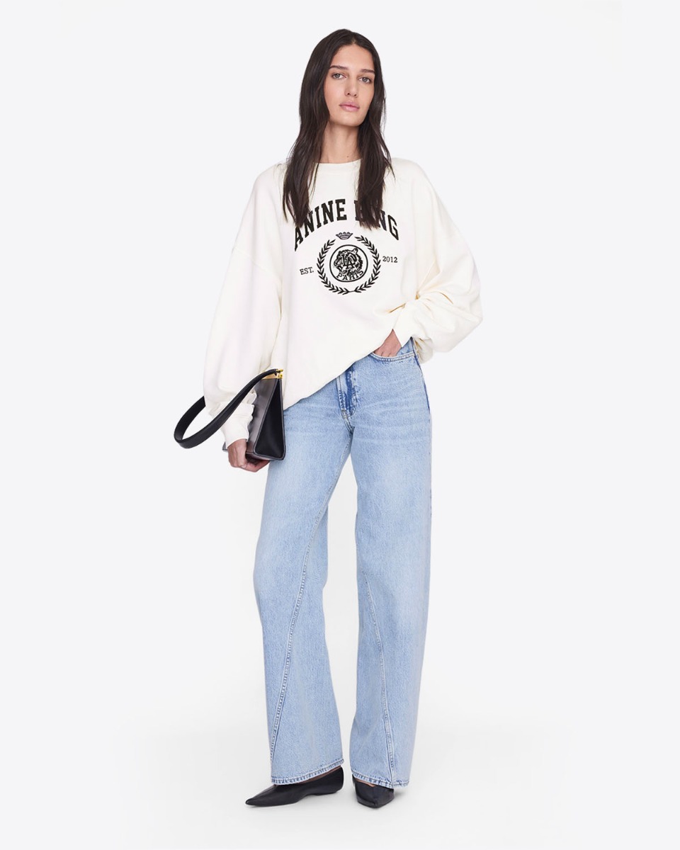 Sweat-shirt Miles Anine Bing en coton &eacute;cru s&eacute;rigraphie Coll&egrave;ge devant, port&eacute; avec un jean bleu ciel taille haute.