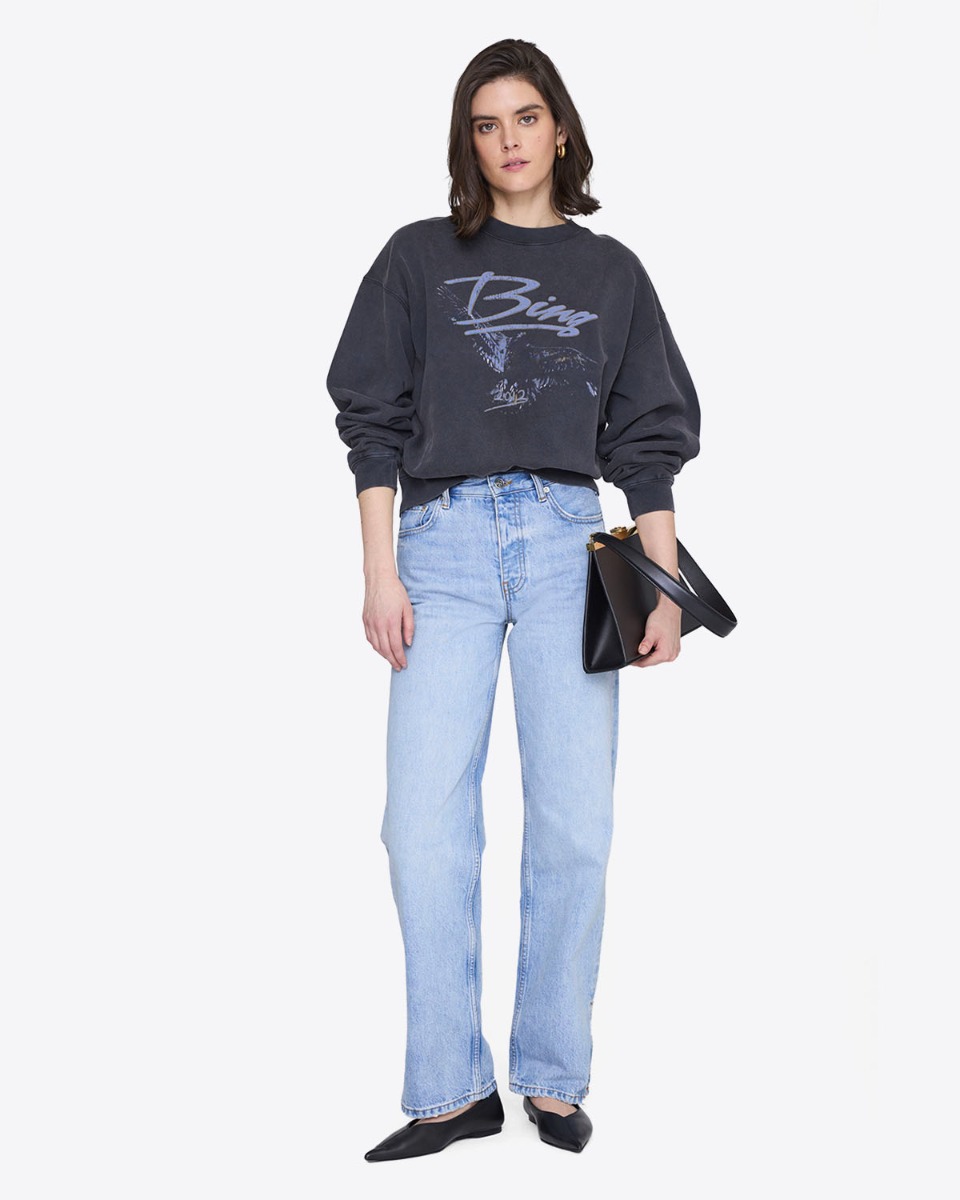 Sweat-shirt Spencer Anine Bing en coton noir d&eacute;lav&eacute; s&eacute;rigraphie aigle et logo Bing bleu, port&eacute; de face avec un jean bleu ciel taille haute.