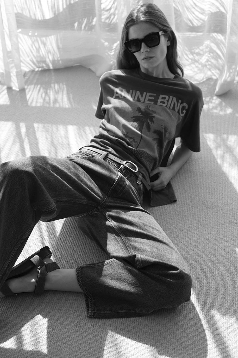 T-shirt manches courtes Cade Palms Anine Bing en jersey de coton fluide noir d&eacute;lav&eacute; s&eacute;rigraphie avec les palmiers mythique de Los Angeles fond bleu et logo &laquo; ANINE BING &raquo;, port&eacute; de face avec un jean large.