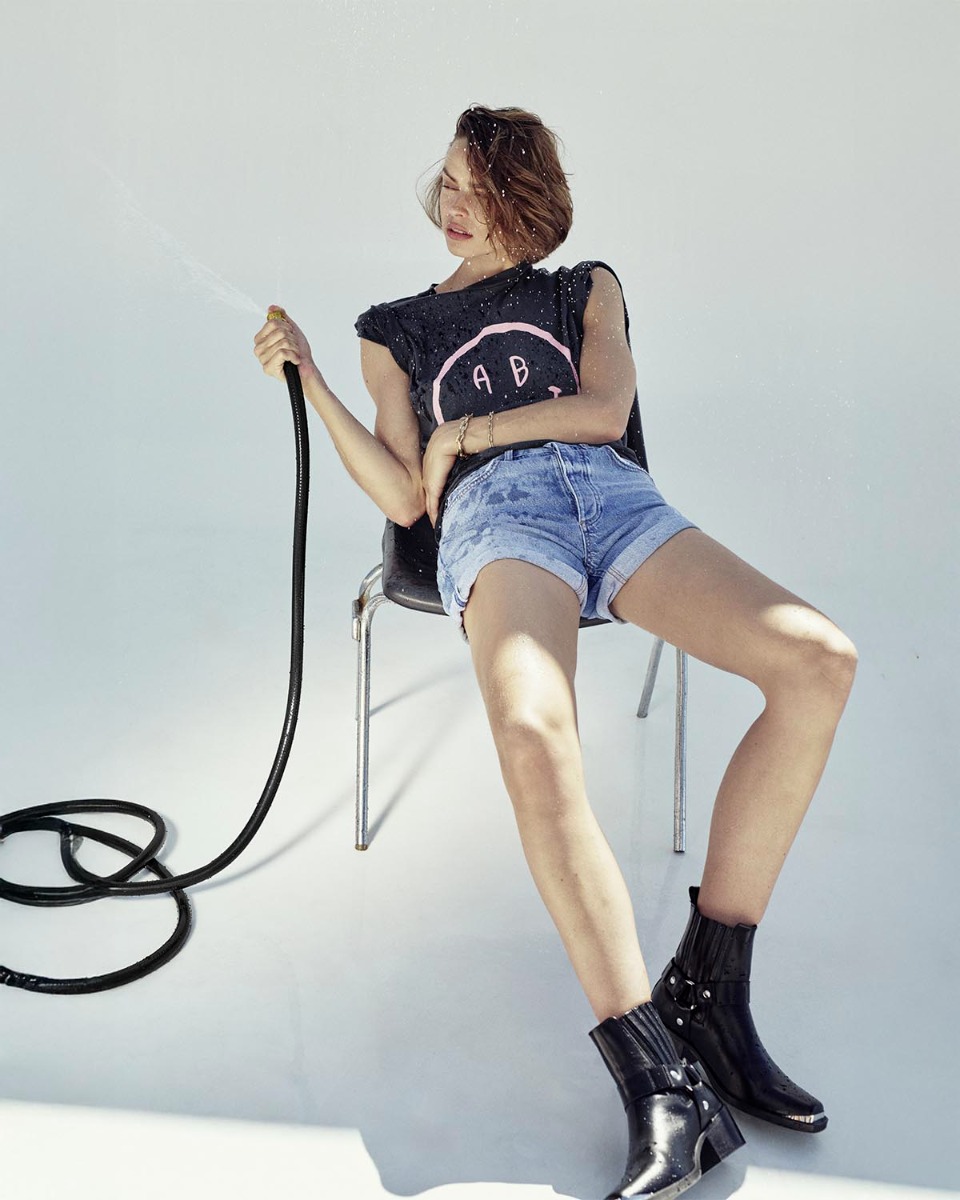 Tee-shirt manches courtes Cade Anine Bing en coton gris d&eacute;lav&eacute; s&eacute;rigraphie rose smiley &laquo; AB &raquo; sur le devant, port&eacute; de face avec un short en denim et des boots de biker.