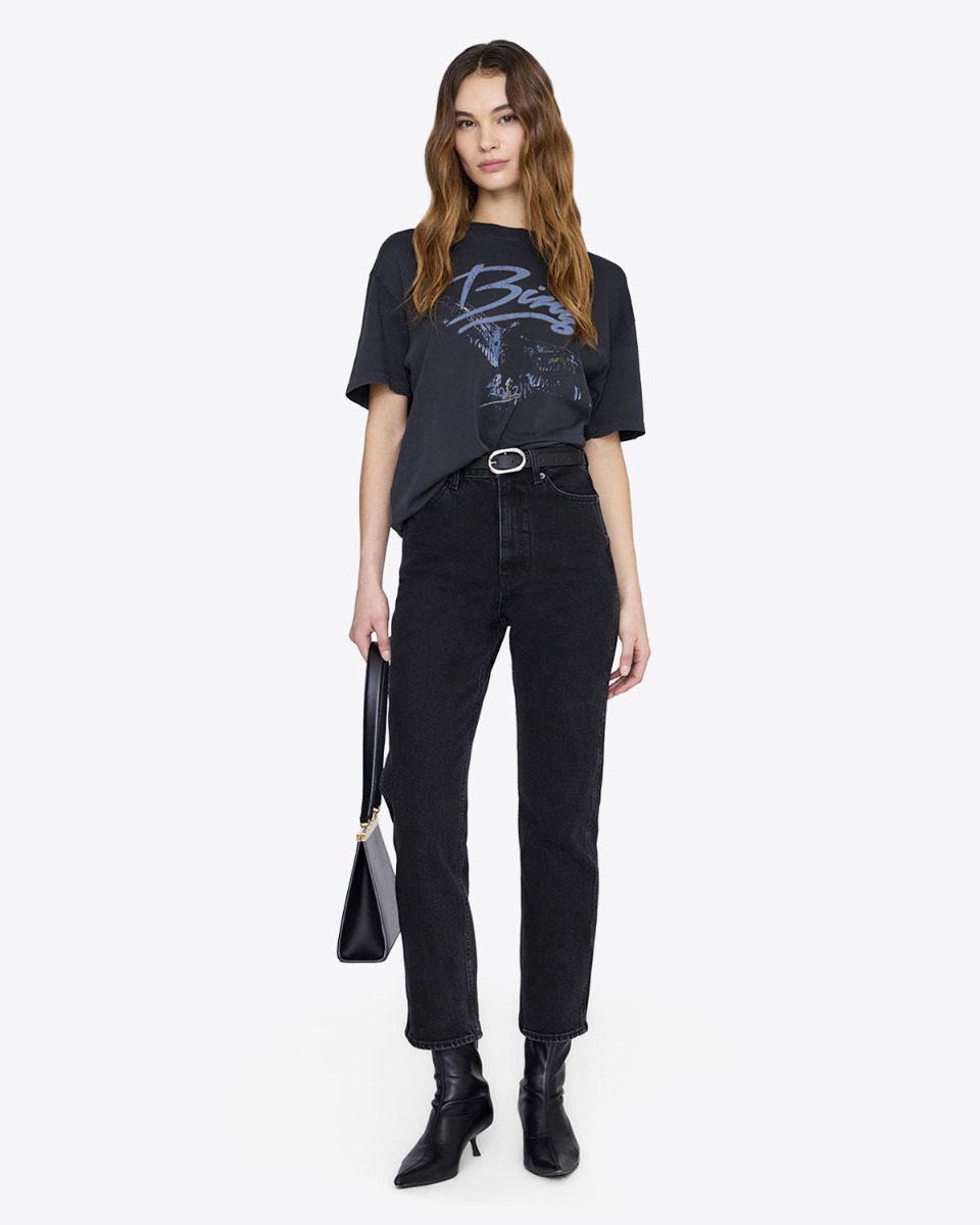 T-shirt manches courtes Kent Eagle Anine Bing en coton noir d&eacute;lav&eacute;, s&eacute;rigraphie aigle et logo &laquo; Bing &raquo; bleu, port&eacute; de face avec un jean taille haute noir Anine Bing.