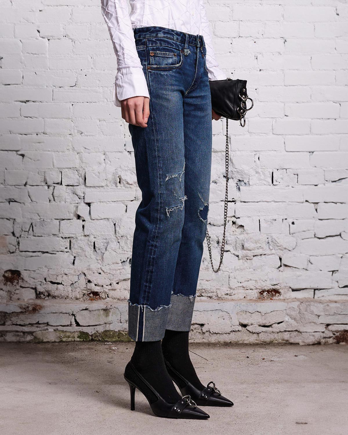Jeans Boy Straight en denim bleu avec des accros rapiécés et un grand revers sur le bas de la jambe R13. Porté avec des escarpins.