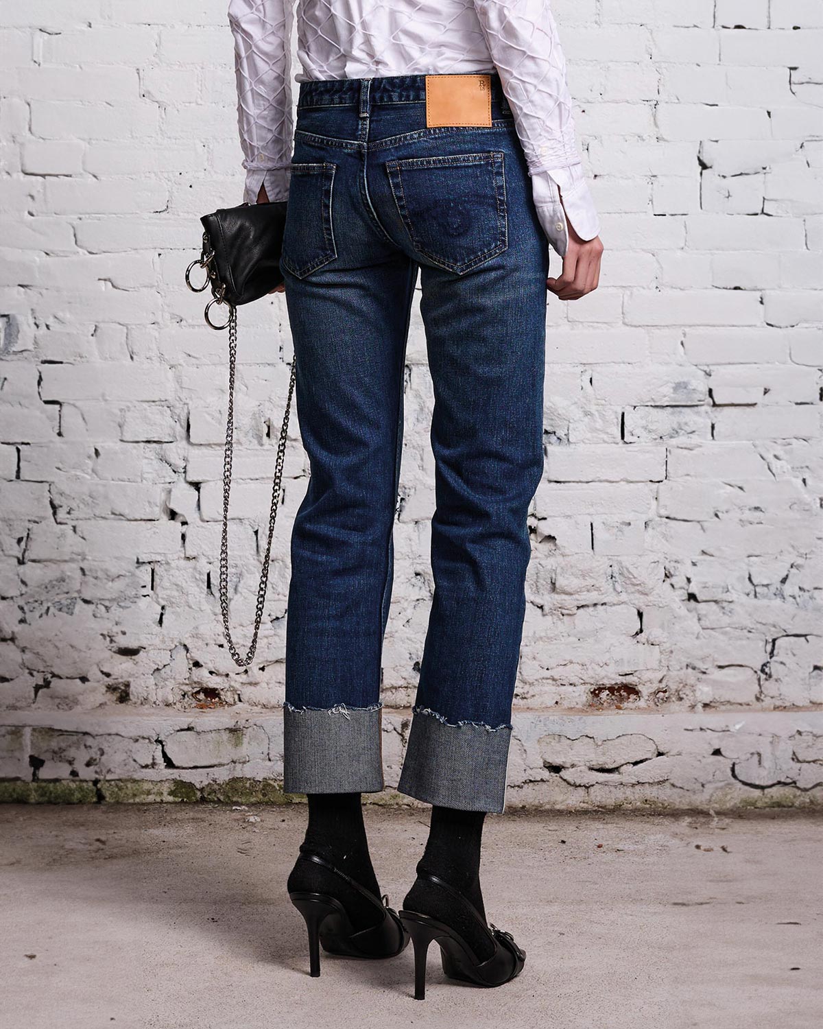Jeans Boy Straight en denim bleu avec des accros rapiécés et un grand revers sur le bas de la jambe R13. Porté de dos.