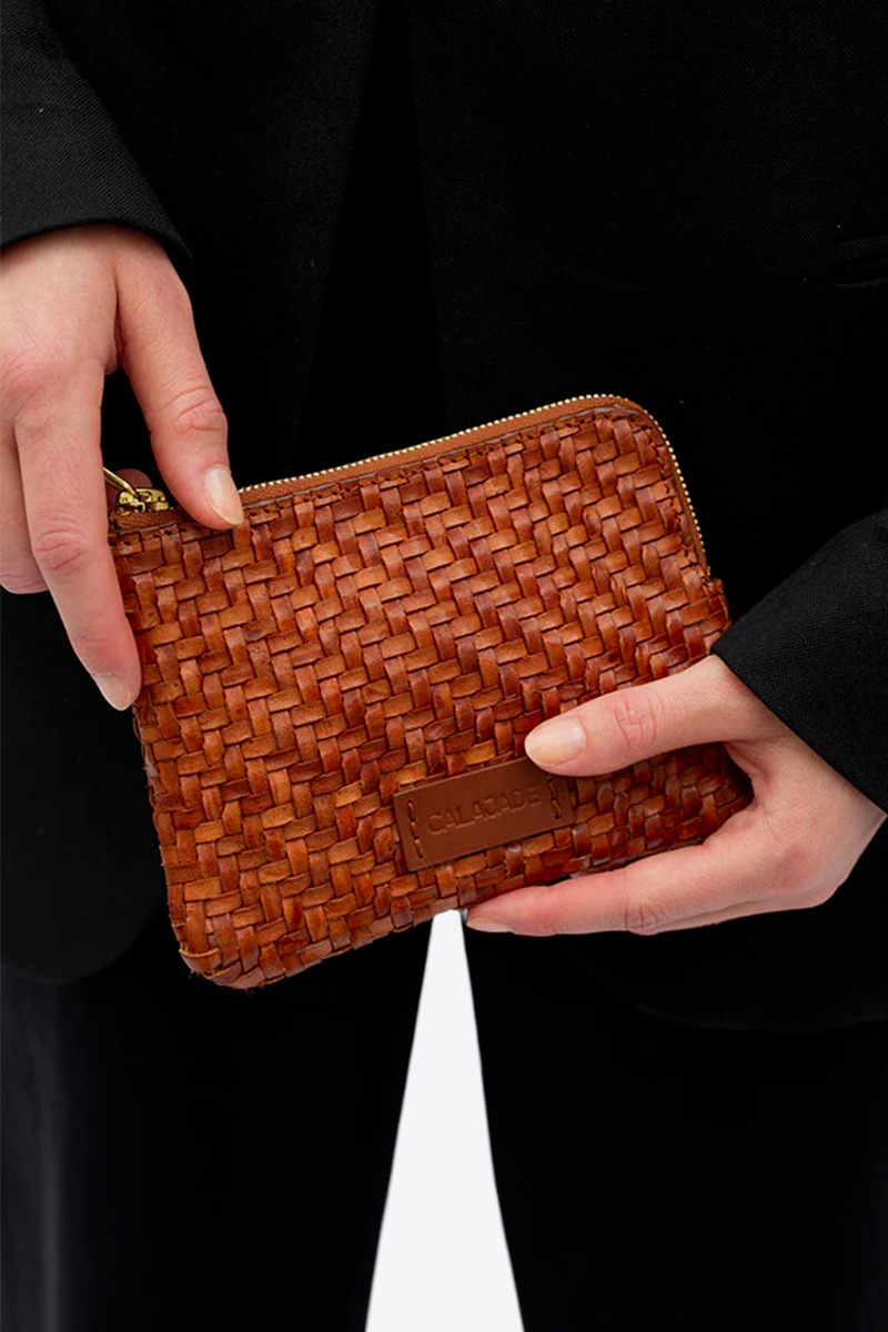 Pochette Batu XS Cala Jade en cuir tress&eacute; Nutmeg cognac, port&eacute;e dans les mains.