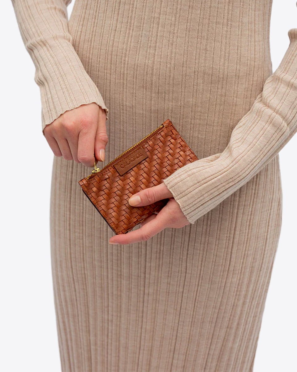 Portefeuille Caia Cala Jade en cuir tress&eacute; Nutmeg cognac port&eacute; dans les mains.