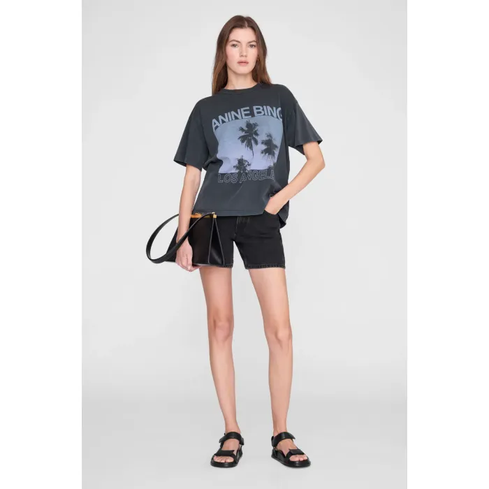 T-shirt manches courtes Cade Palms Anine Bing en jersey de coton fluide noir délavé sérigraphie avec les palmiers mythique de Los Angeles fond bleu et logo ANINE BING, porté de face avec un short.