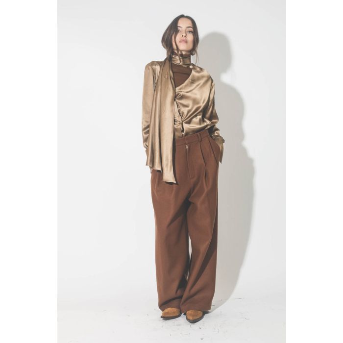 Chemise manches longues drapée col écharpe en satin de soie camel doré. Porté avec un pantalon à pinces en drap de laine marron.