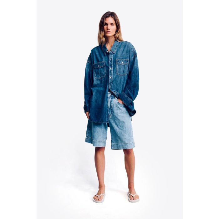 Short long Keaton Relaxed Denimist en denim « Stone Wash Blue », porté de face avec une chemise en jean bleu foncé.