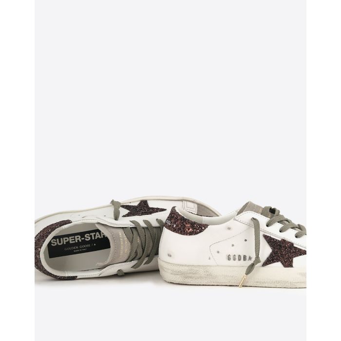 Sneakers Superstar Golden Goose femme en cuir blanc avec étoile et talon arrière à paillettes marron. Détail du logo GGDB en lettres métalliques argentées sur le côté.