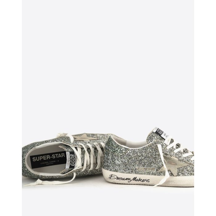 Sneakers Superstar Golden Goose femme à paillettes argentées avec des reflets verts, étoile en cuir lisse doré. Détail du graffiti sur la semelle " Dream Makers ". 