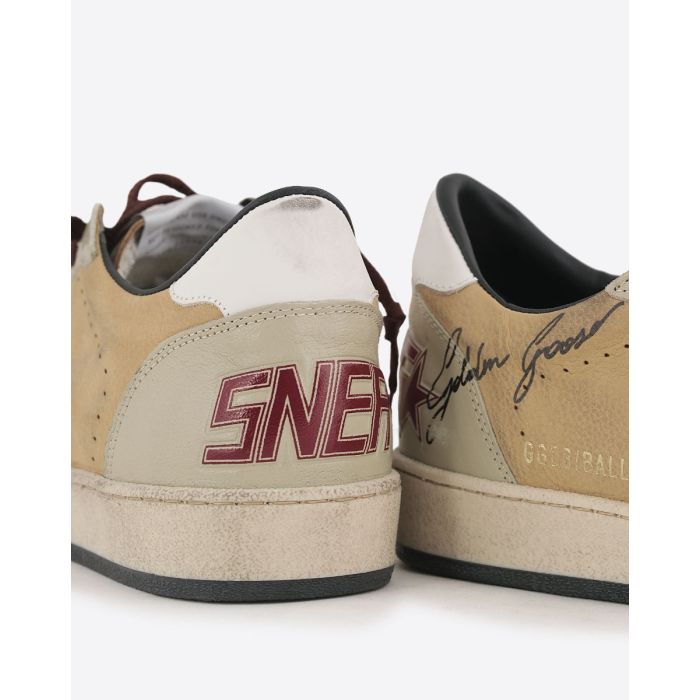 Sneakers Ball Star Golden Goose homme en cuir beige, empiècement écru, étoile blanche arrière blanc. Signature volontairement usé "Golden Goose" effet graffiti sur le côté. Lacets bordeaux. Détail du renfort arrière. 
