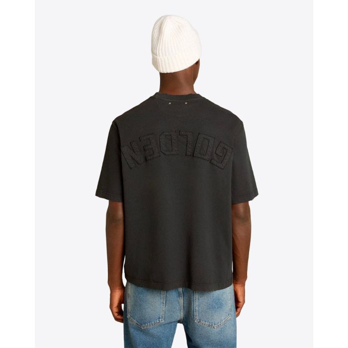 Tee-shirt Relaxed Fit Golden Goose Unisexe en coton noir logo « GOLDEN » inversé dans le dos, porté de dos avec un bonnet.