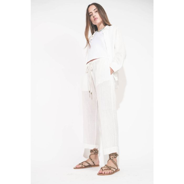 Sandales plates avec brides Zenobie K.Jacques St-Tropez en cuir "pony" léopard. Porté de profil avec un chemise en voile de coton blanc et un pantalon assorti en voile de coton blanc The Great. 