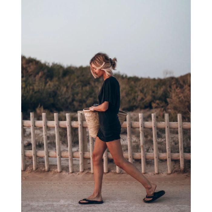 Robe courte drapée Mikuta en jersey noir, portée de profil avec un panier en osier.