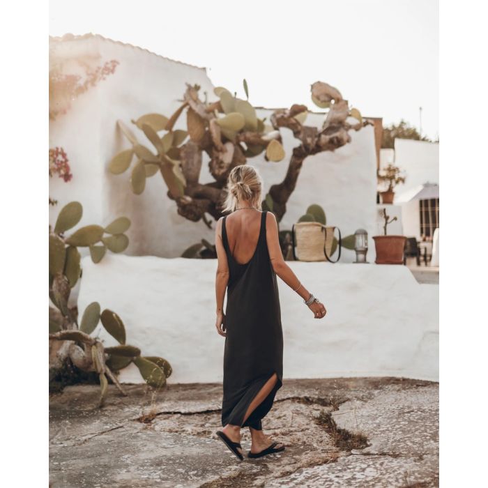 Robe longue dos nu Mikuta en jersey noir, portée de dos avec des sandales noires.