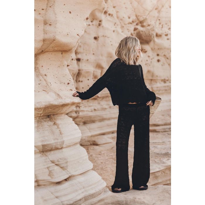 Pantalon en crochet noir en lin et coton Mikuta. Porté avec un pull en crochet noir assorti et des sandales noires.