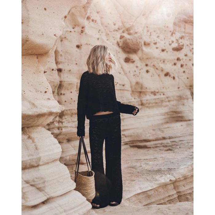 Pantalon en crochet noir en lin et coton Mikuta. Porté avec un pull en crochet noir assorti et un panier en osier.
