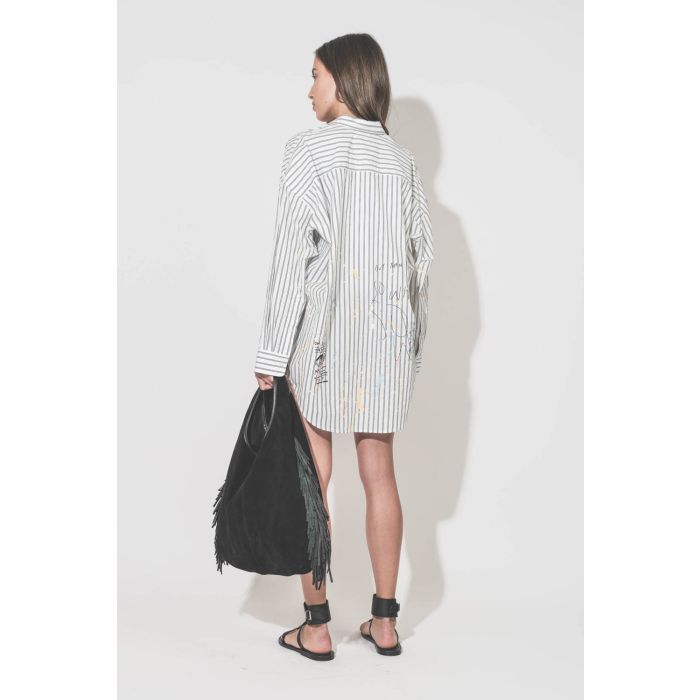 Chemise oversized en popeline blanche à rayures noires et graffiti Drop Neck R13. Portée de dos avec des sandales noires Caravelle K.Jacques St Tropez et un sac à franges Paco Jérôme Dreyfuss.