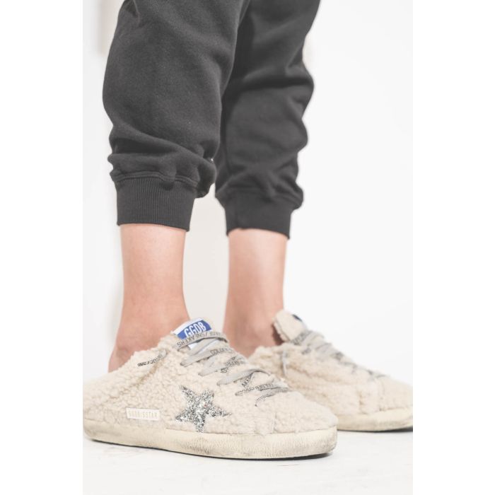 Pantalon de jogging taille basse à nouer sur les hanches resserré en bas bord côte noir The Cropped Sweatpant The Great. Détail du bas. Porté avec des sneakers Super Star sabot en fourrure écru 10757 Golden Goose. 