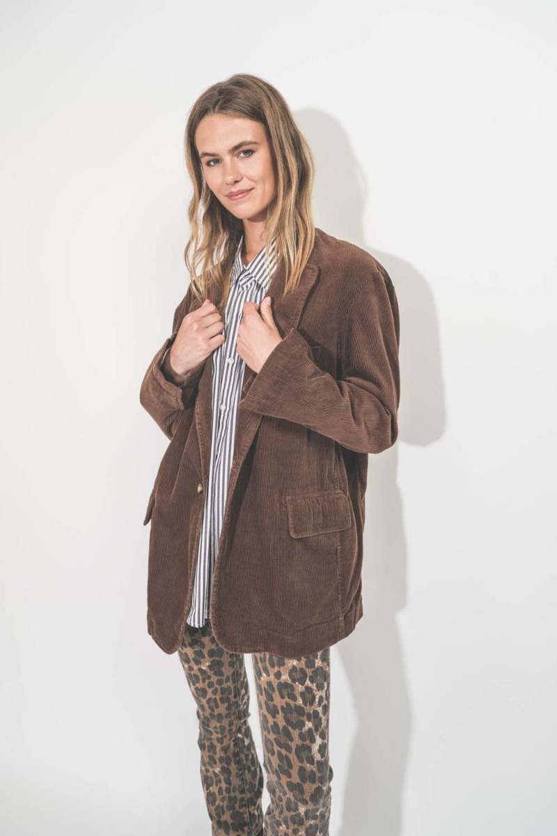 Veste oversize deconstructed Denimist en velours côtélé marron. Portée de profil avec une chemise à rayures. 