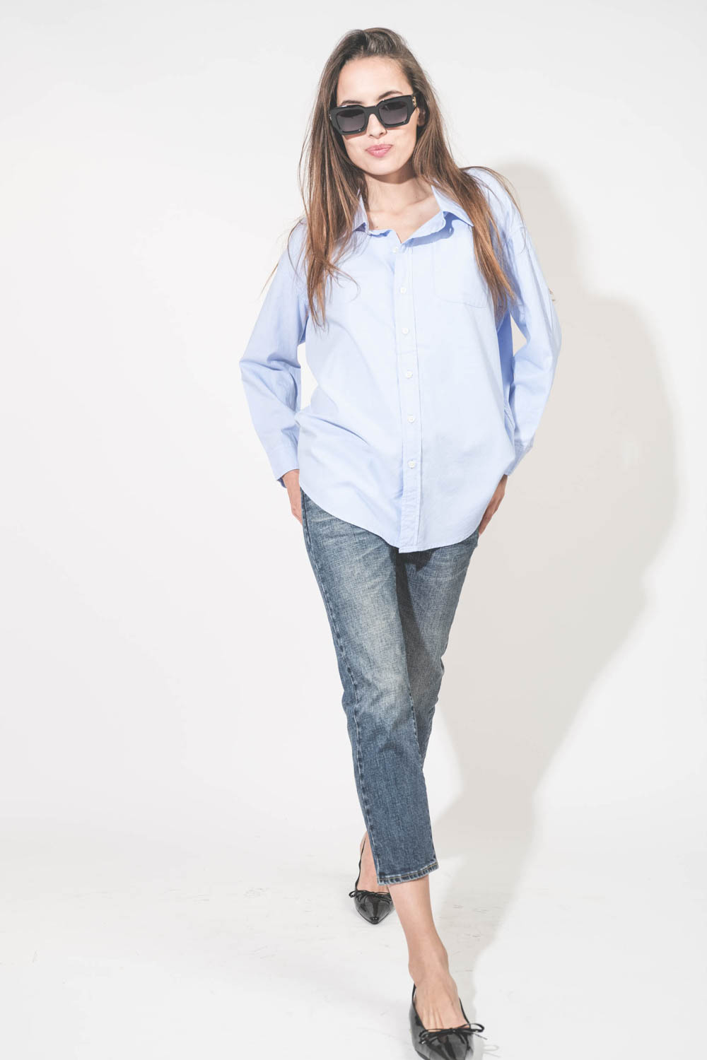 Chemise oxford classique plus longue derrière que devant Button Front bleu ciel Denimist. Porté avec un jean Boy Straight Mire Blue Stretch R13 et des ballerines en cuir noir vernis Slingback Hells Zoey Anine Bing. Lunettes de soleil montures noires Indio