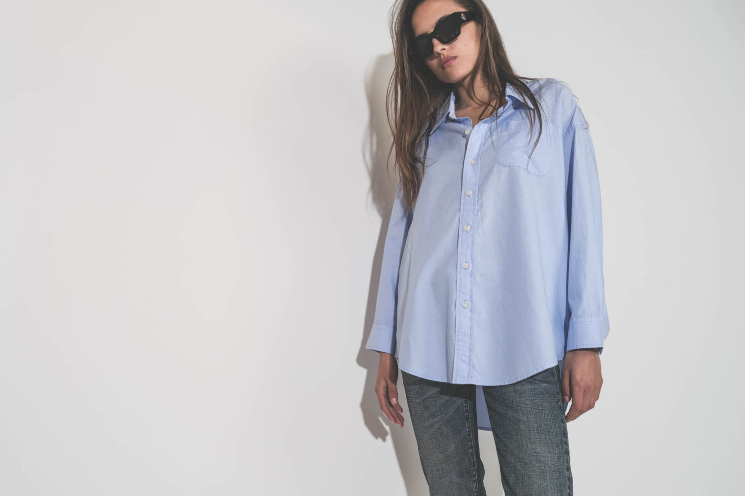Chemise oxford classique plus longue derrière que devant Button Front bleu ciel Denimist. Porté de face avec un jean Boy Straight Mire Blue Stretch R13. Lunettes de soleil montures noires Indio logo AB Anine Bing.