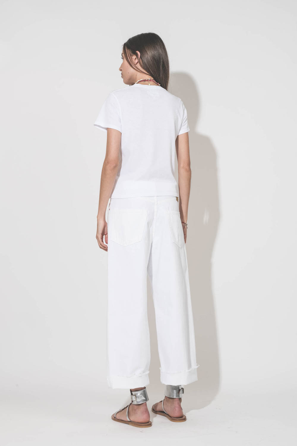 Jean large taille basse en toile blanche lavée Georgia Denimist. Porté de dos avec un tee-shirt Little blanc The Great et des sandales Caravelle en cuir argent K.Jacques Saint-Tropez. Bijoux Isabel Marant.