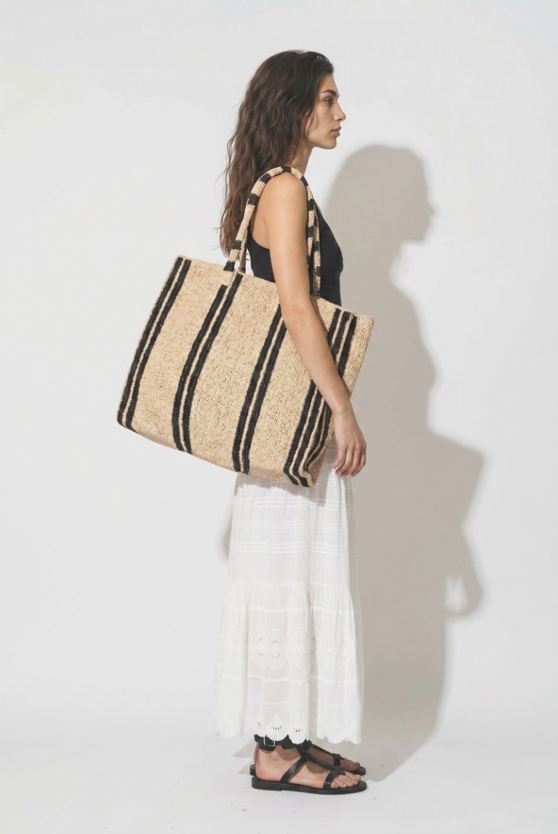 Grand Cabas Raffia Weekender Vacation Road Gabriele Frantzen en raphia rayé écru et noir, porté de profil à l'épaule.