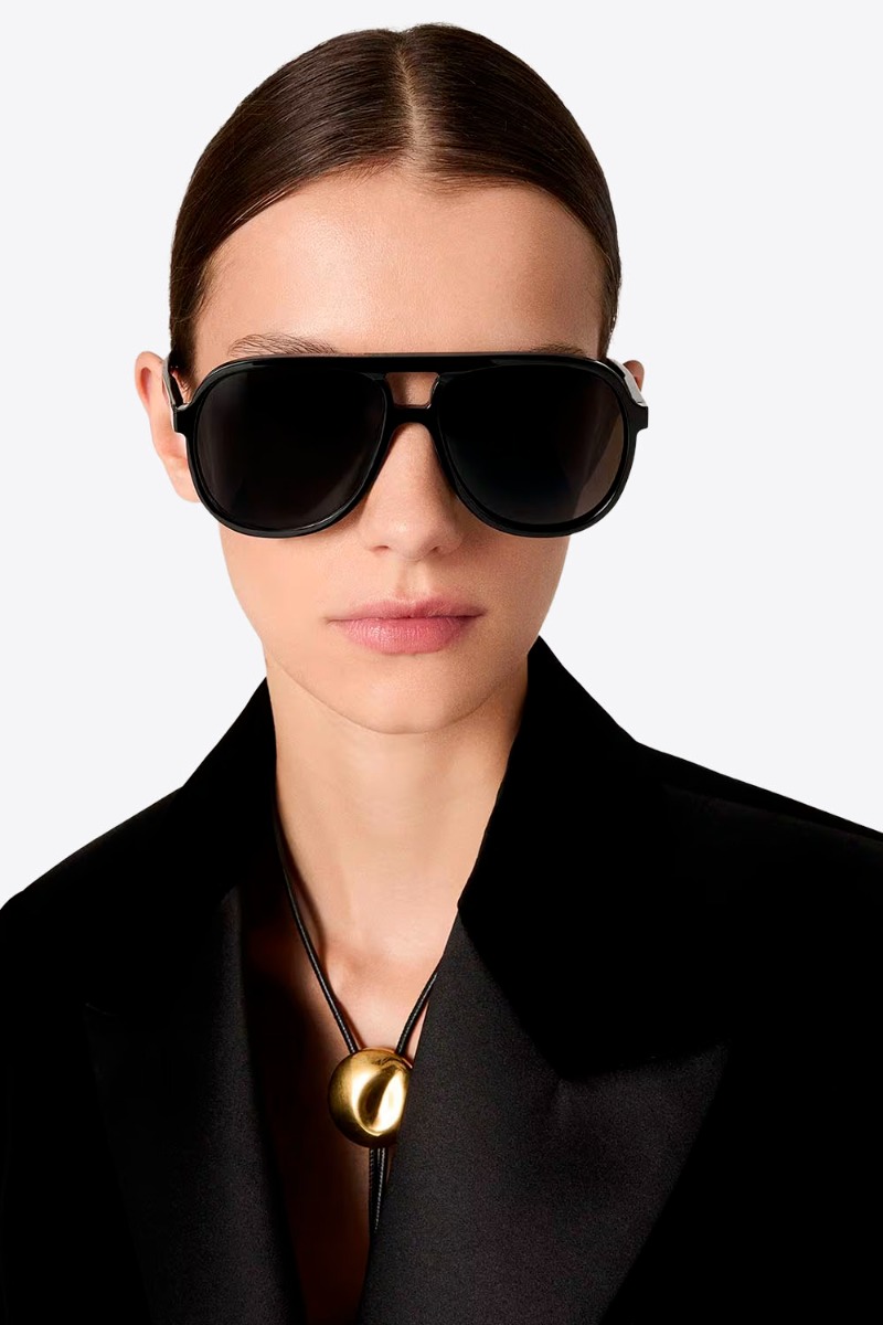Lunettes de soleil Charlie Golden Goose unisexe. Montures aviateur noires, port&eacute;es de face par une femme.