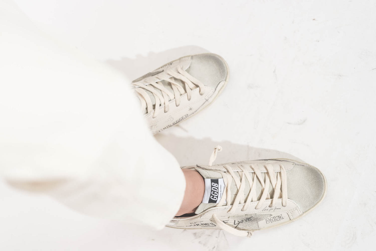 Sneakers en cuir blanc Graffiti écritures et dessins noirs arrière en cuir argent Golden Goose femme. Edition limitée. Portées avec un jean Boy Straight écru stretch R13.