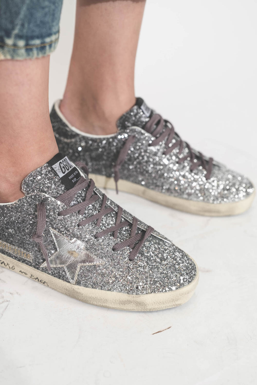 Sneakers entièrement recouvertes de paillettes argentées et noires, étoile en cuir lisse tague écritures noires sur la semelle droite beige "LOVE You To The Star And Back"  Super-star Golden Goose femme. Portées de profil avec un jean Boy Straight bleu R1