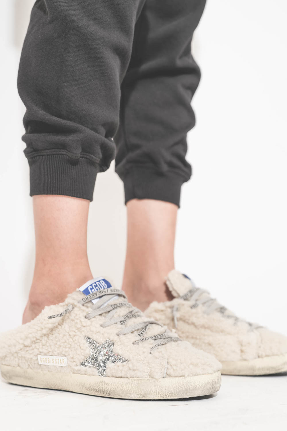 Sneakers sabot en fourrure de mouton retournée écru étoile à paillettes argentées 10757 Super-Star Sabot Golden Goose femme. Portées avec un bas de jogging Cropped noir The Great.