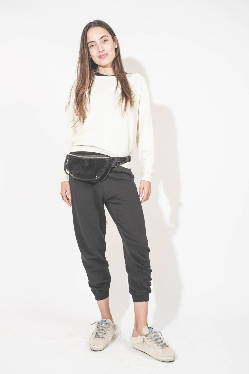 Sneakers sabot en fourrure de mouton retournée écru étoile à paillettes argentées 10757 Super-Star Sabot Golden Goose femme. Portées avec un sweat-shirt écru Shrunken et un bas de jogging Cropped noir The Great. Sac banane en cuir noir Lino Jérôme Dreyfus