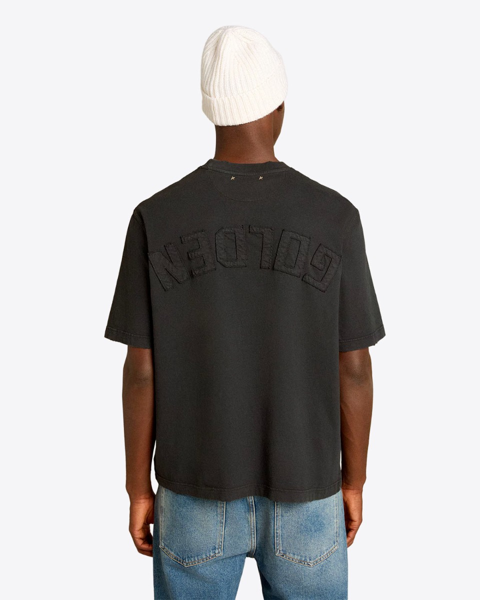 Tee-shirt Relaxed Fit Golden Goose Unisexe en coton noir logo &laquo; GOLDEN &raquo; invers&eacute; dans le dos, port&eacute; de dos avec un bonnet.