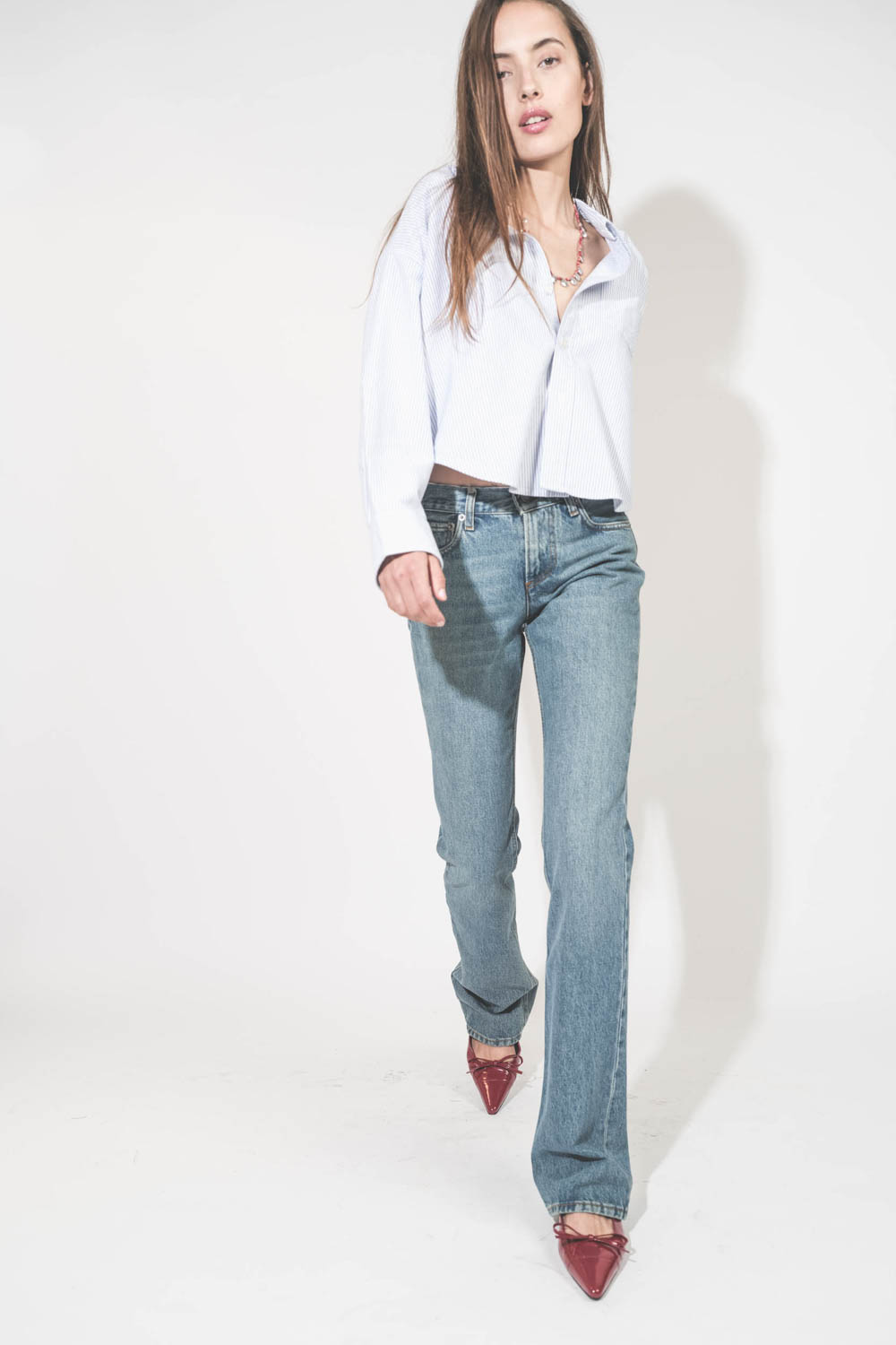 Jean droit taille basse et long bleu délavé Carly Haikure. Porté avec une chemise courte à rayures bleues Button Front Denimist et des ballerines rouge Zoey Anine Bing. Collier Adriel rouge Isabel Marant.