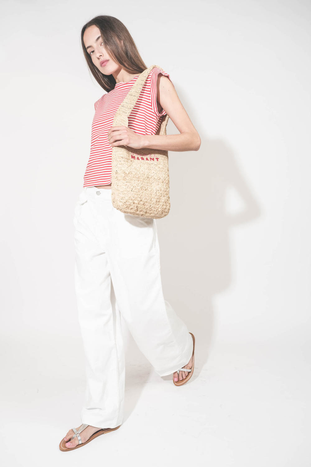 Jean large à pinces taille basse en toile blanche Candy Twill Haikure. Porté de profil avec un tee-shirt rayé rouge et blanc The Great et un panier en osier Isabel Marant. 