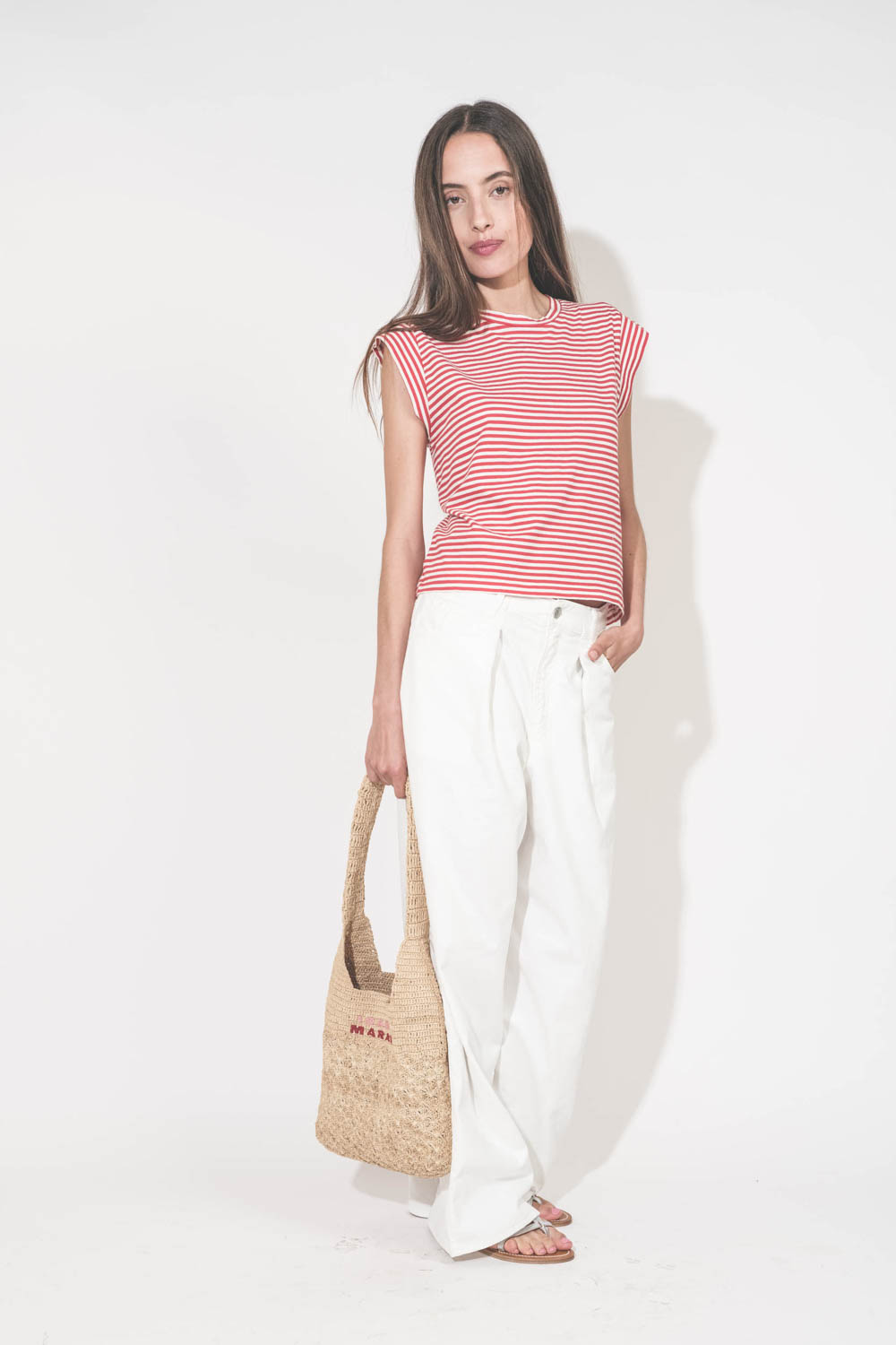 Jean large à pinces taille basse en toile blanche Candy Twill Haikure. Porté de face avec un tee-shirt rayé rouge et blanc The Great. Un panier en osier Isabel Marant et des sandales en cuir argent K.Jacques St Tropez.