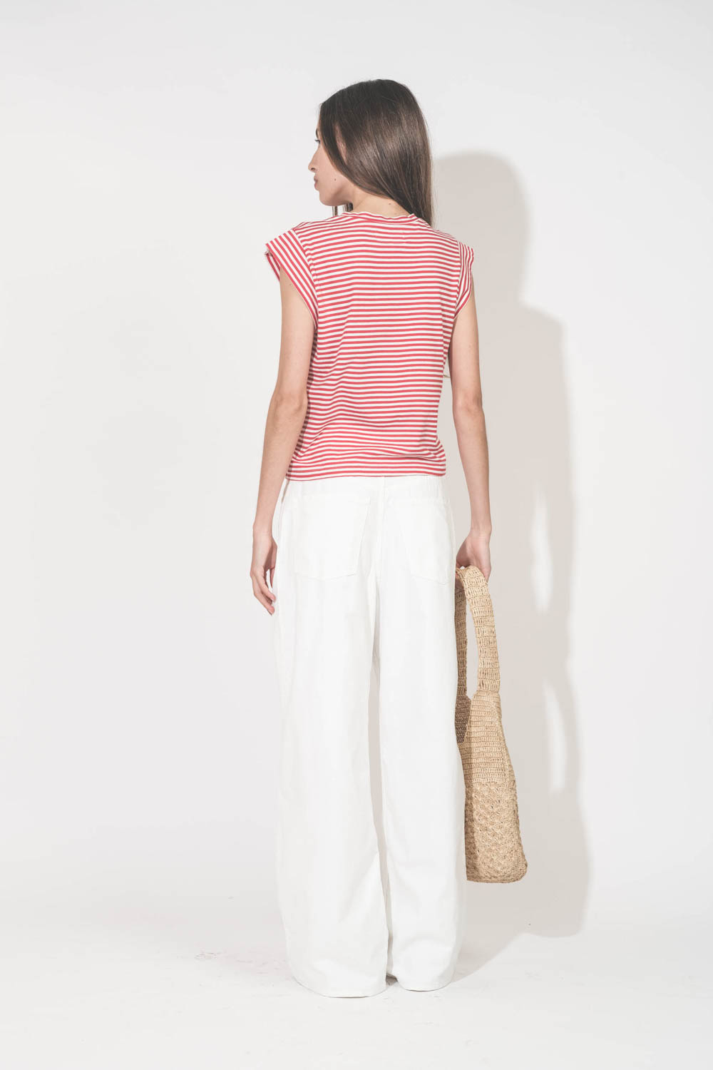 Jean large à pinces taille basse en toile blanche Candy Twill Haikure. Porté de dos avec un tee-shirt rayé rouge et blanc The Great. 