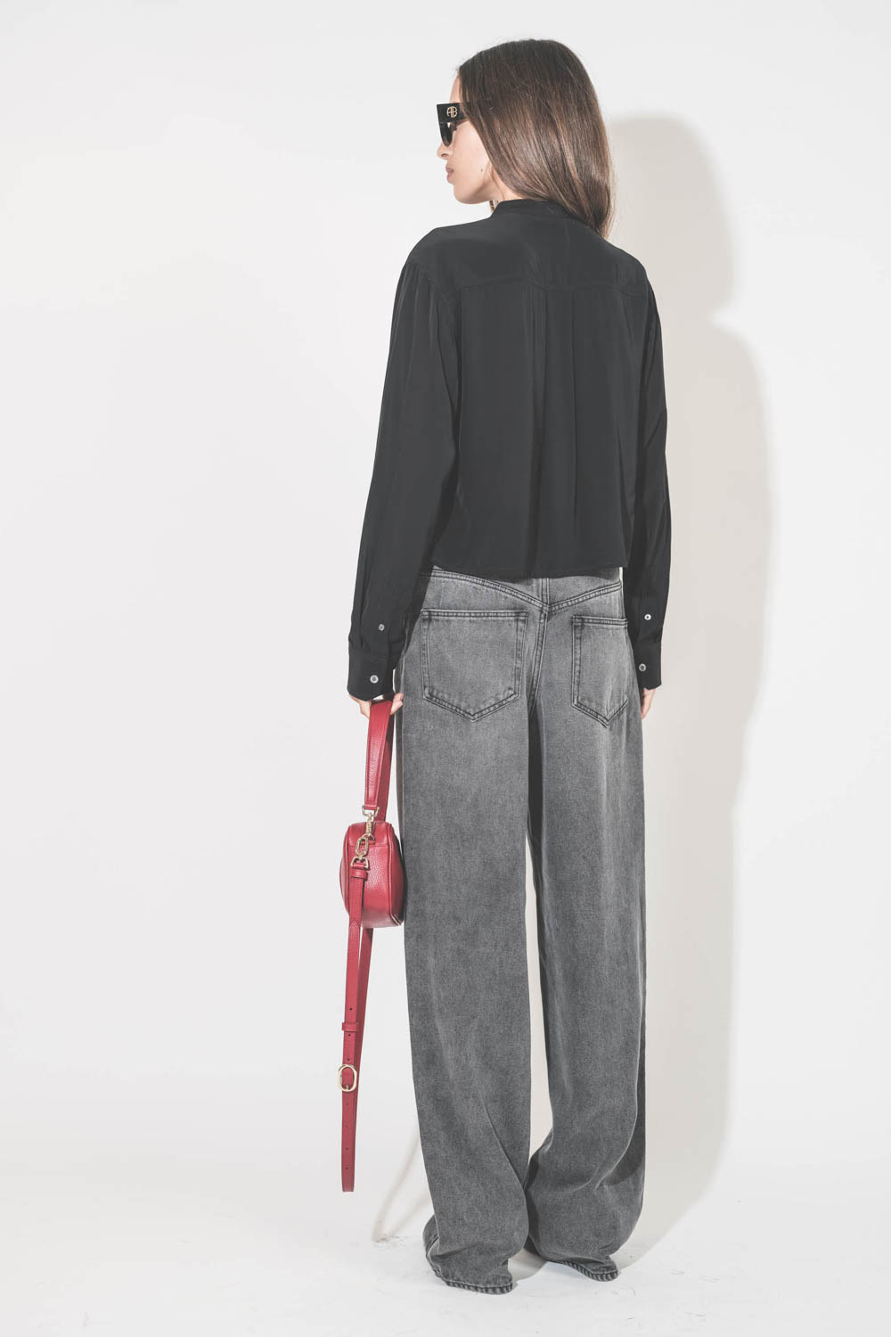 Chemise courte manches longue col Mao plis devant en viscose noire Adzara Marant Etoile. Portée de dos avec un jean large fluide gris clair Joanny Marant Etoile et des escarpins en cuir noir Slingbacks à talons Freya Anine Bing. Sac en cuir rouge logo AB 