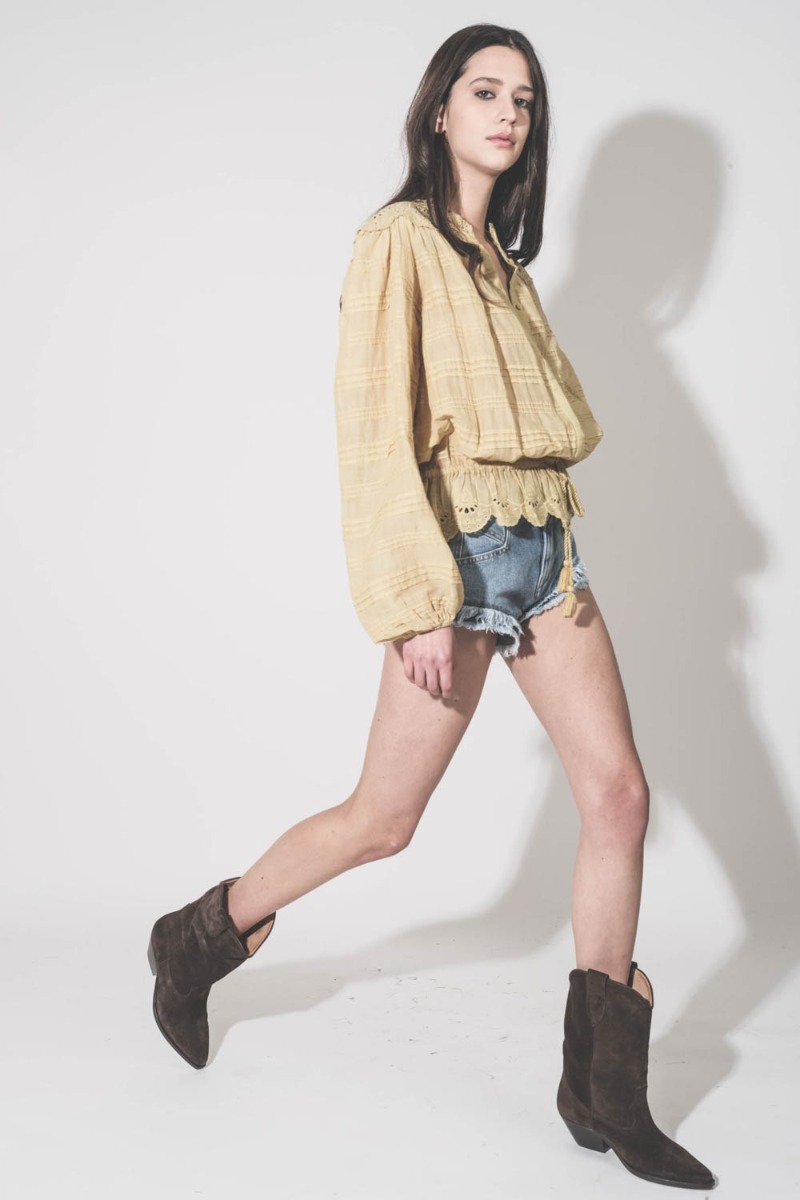 Chemise Polly Isabel Marant &Eacute;toile en voile de coton et en dentelle fleurie ocre, port&eacute;e de profil avec un short en jean et des santiags.