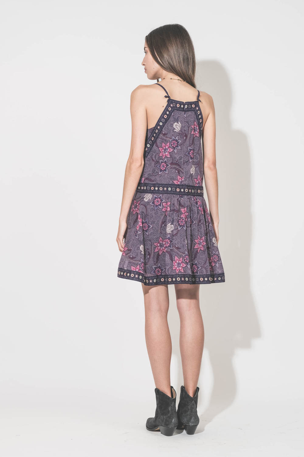 Robe au dessus du genoux fines bretelles en voile de coton imprimé fleurs violettes doublée Daniella Isabel Marant Etoile. Portée de dos avec des boots en cuir suédé noir délavé Dewina Isabel Marant et un collier tibétain Sharing. 