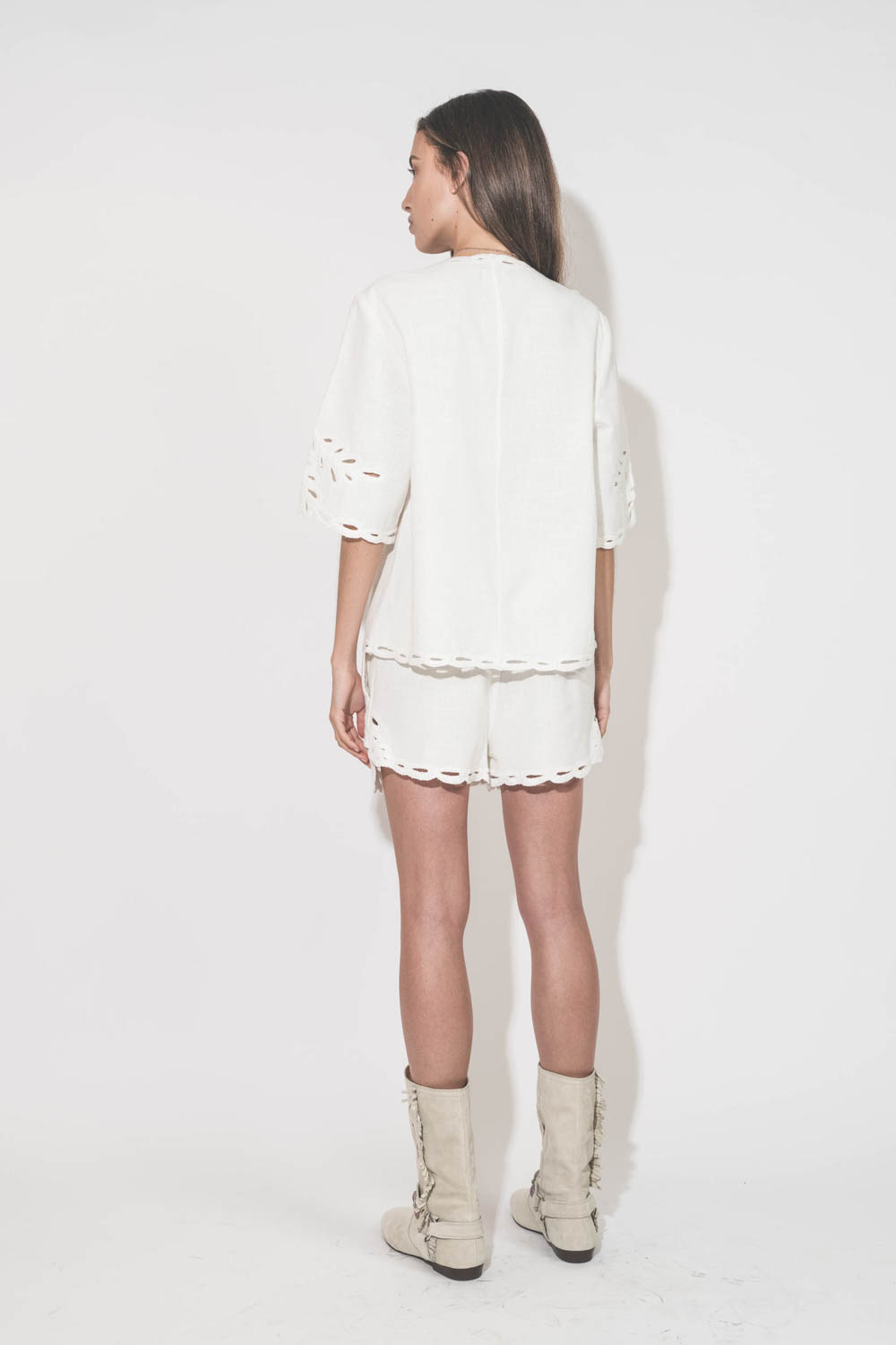 Short court en coton texturé et dentelle Safa Isabel Marant Etoile. Porté de dos avec un top assorti Shana blanc Isabel Marant Etoile et des bottes en cuir suédé et brodé écru Siani Isabel Marant. Collier croix De Jaegher et bague en cristal Alba Pascale 