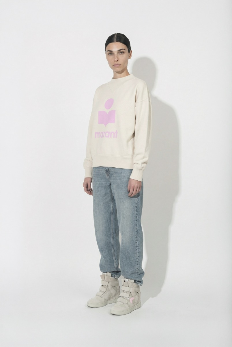 Sweatshirt Moby Isabel Marant &eacute;toile en coton &eacute;cru et logo rose sur le devant, port&eacute; de profil avec un jean bleu et des baskets IM3 Isabel Marant.