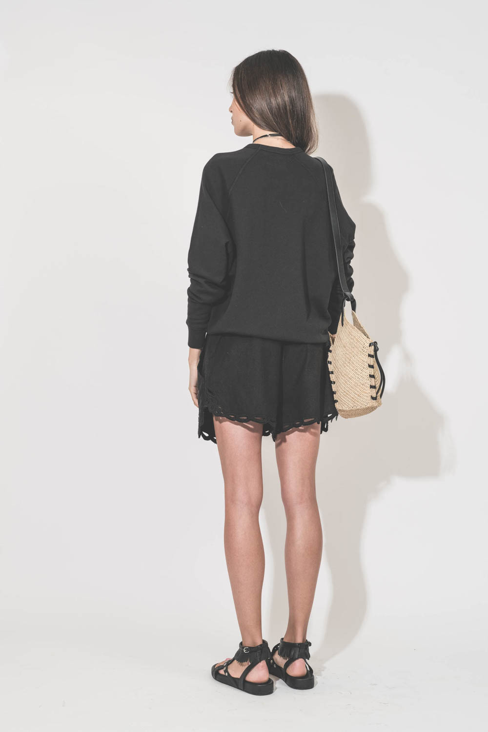 Panier en osier naturel à bandoulière en cuir noir réglable Tampa Mini Isabel Marant. Porté de dos avec un sweat-shirt classique noir College The Great et un short court en coton et dentelle ajourée noire Safa Marant Etoile. Sandales en cuir noir cloutées